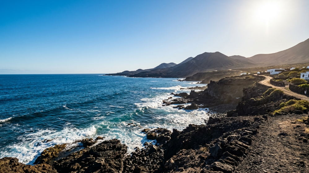 Felsige Vulkanküste mit brechenden Wellen und Bergen im Hintergrund auf Lanzarote
