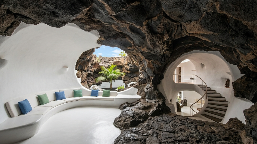 Salotto scavato nella roccia vulcanica con divano curvo e scala nella casa di César Manrique